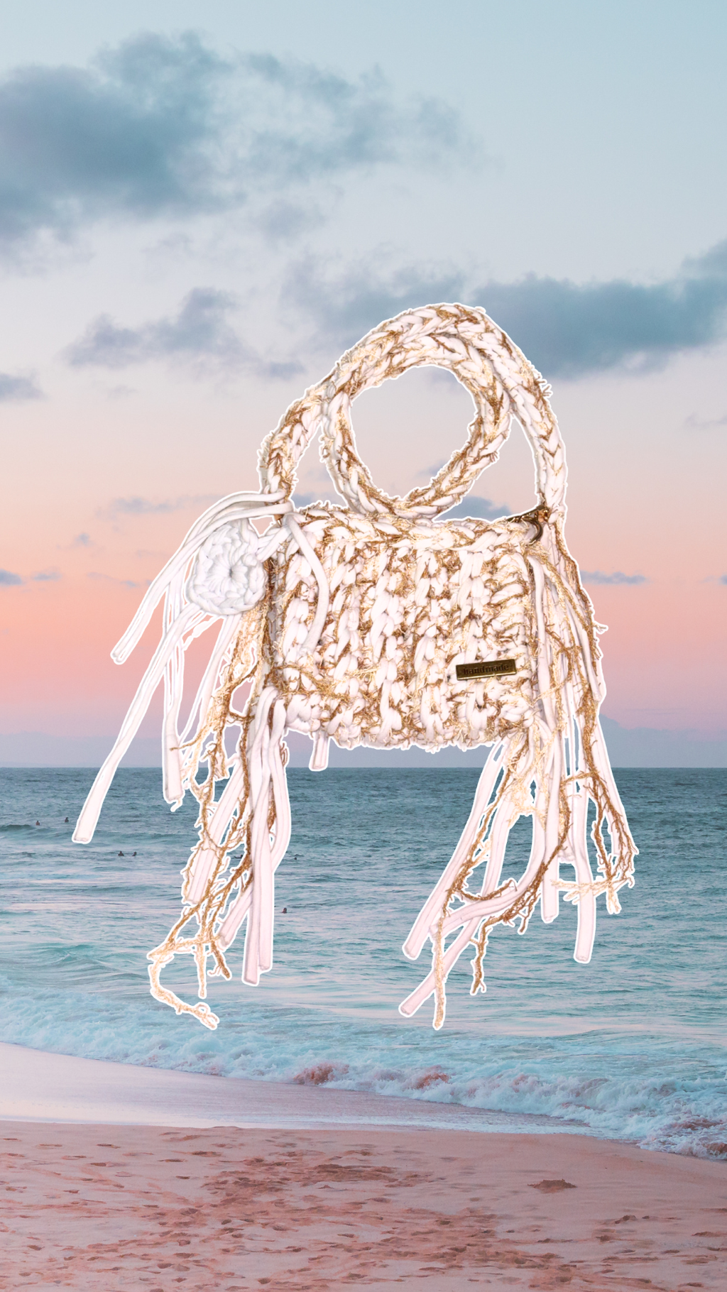 Beige handbag with white fringe on a beach with ocean and sky in the background